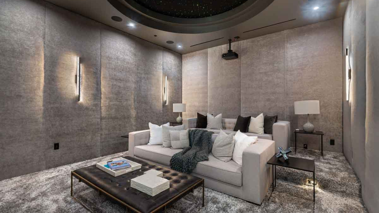 A modern home theater room with plush seating, ambient lighting, and a ceiling projector.